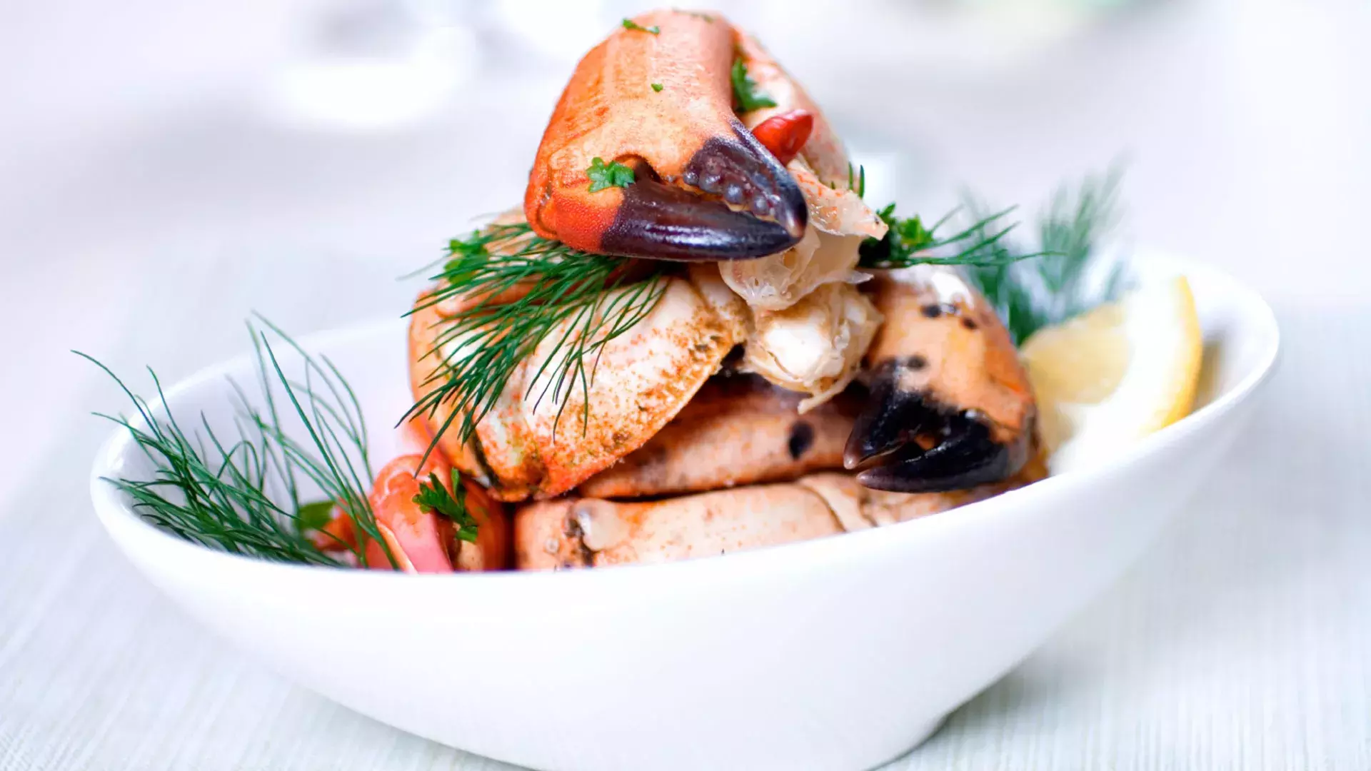 Crab legs are stacked in a white bowl and sprinkled with fresh dill.