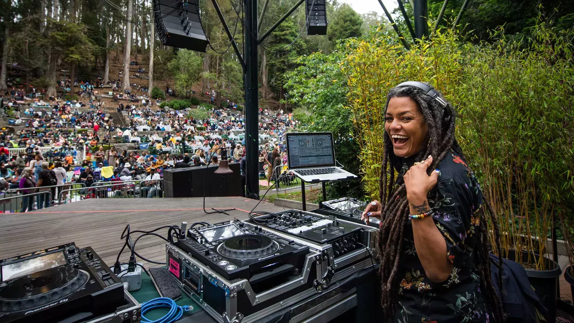 A woman DJing at the Stern Grove Festival looks over her shoulder and smiles into the camera.