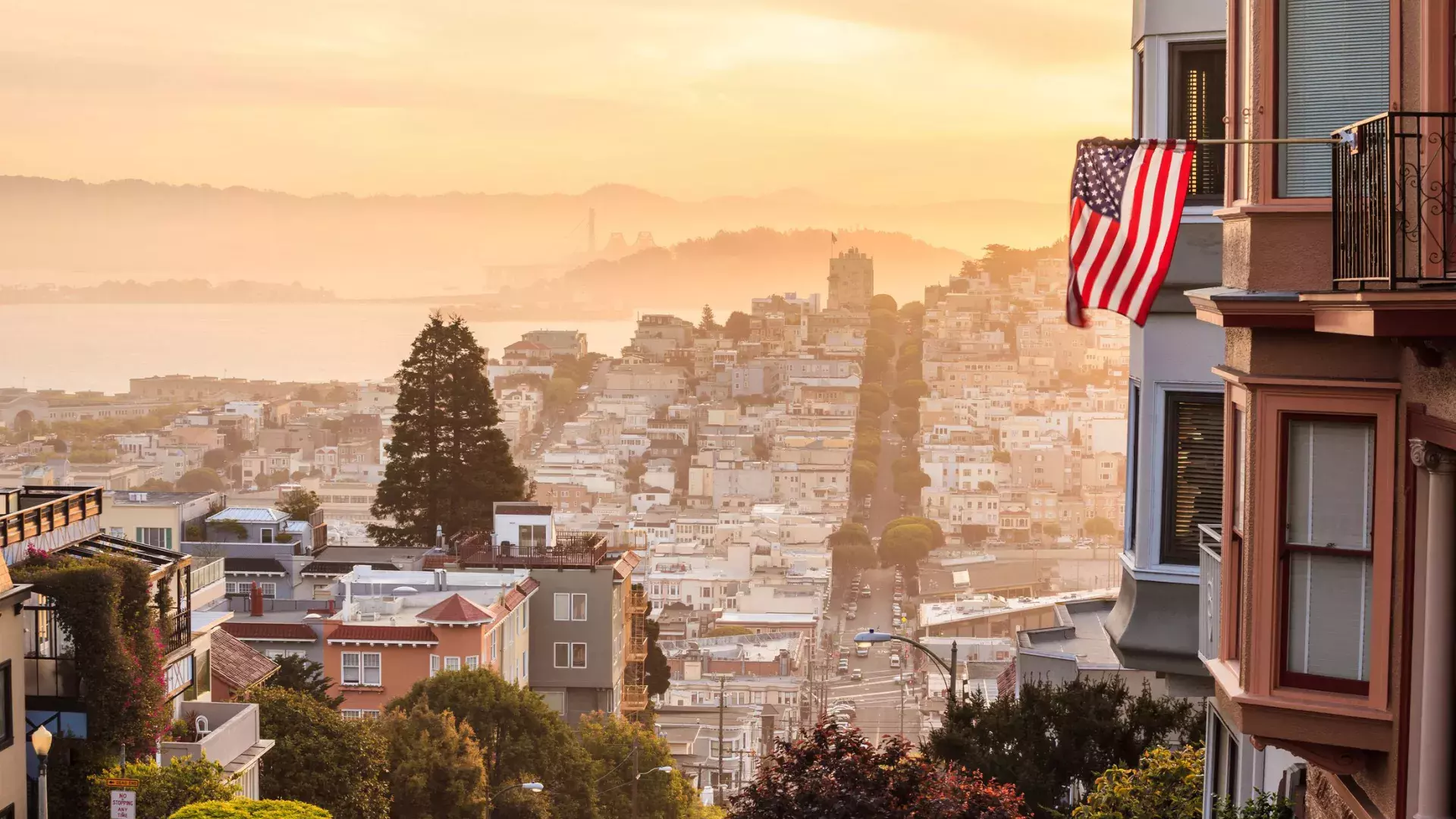 A view of San Francisco from the top of a hill, with an American flag waving in the foreground.