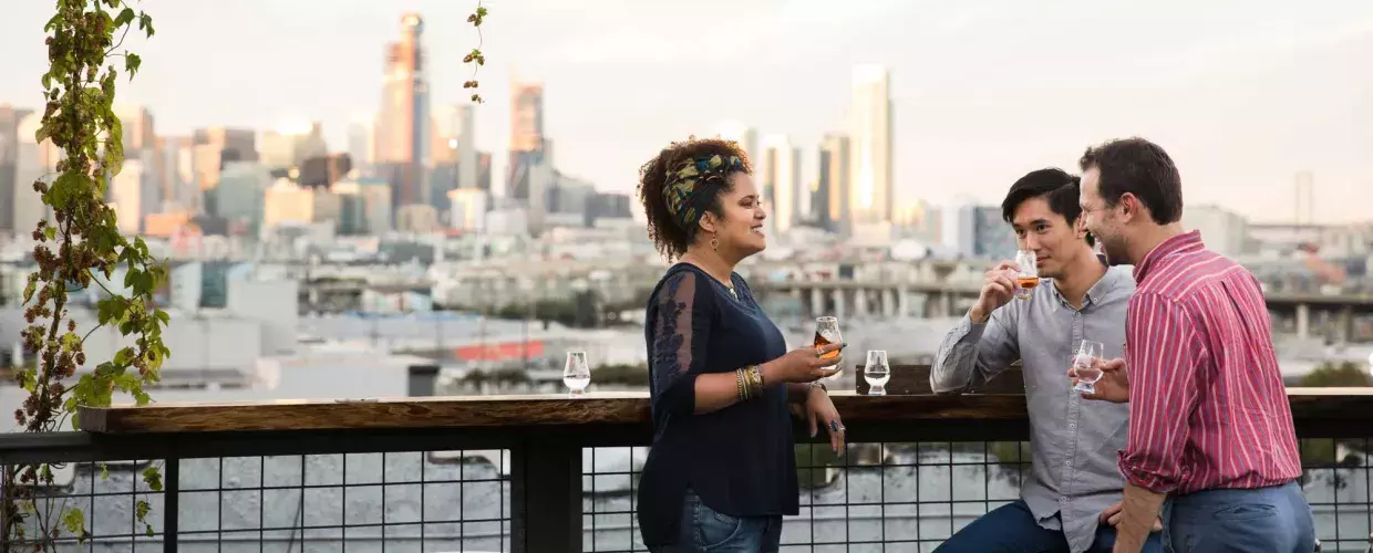 Three people gather around an outdoor table on the roof deck of Anchor Distilling in San Francisco, California.