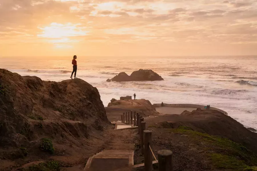 Two people stand on rocks overlooking the ocean at Sutro Baths in San Francisco.