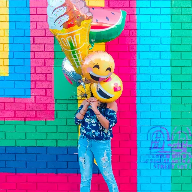 A girl celebrates her birthday with balloons in front of a colorful mural.