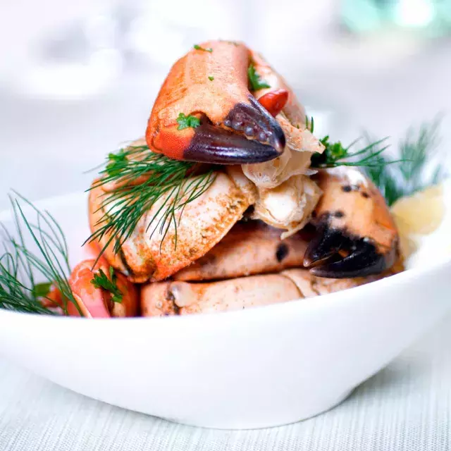 Crab legs are stacked in a white bowl and sprinkled with fresh dill.