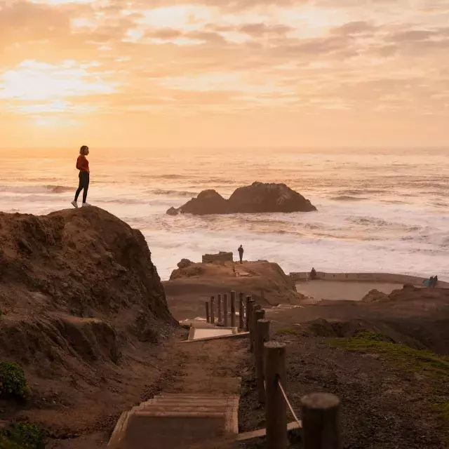 Two people stand on rocks overlooking the ocean at Sutro Baths in San Francisco.